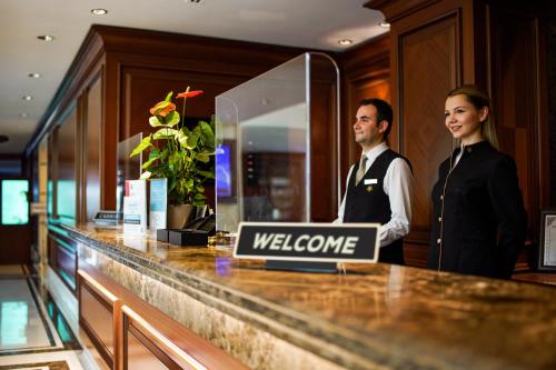 伯薩的住宿－Almira Hotel Thermal Spa & Convention Center，站在柜台上欢迎标志后面的男女