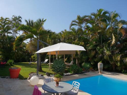 eine Terrasse mit einem Tisch und einem Sonnenschirm neben einem Pool in der Unterkunft la maison du bonheur in Saint-Pierre