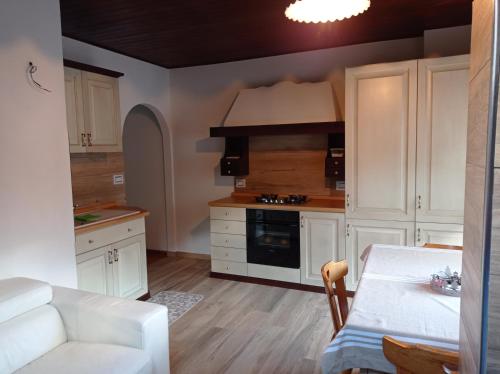 a kitchen with white cabinets and a white table and a table and a couch at La Mansarda di Sabina. in Fiera di Primiero