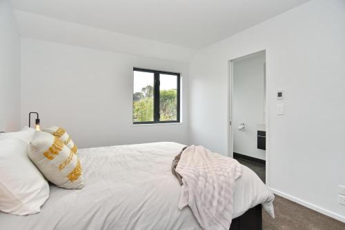 a white bedroom with a bed and a window at Salisbury Style - Modern city apartment - Christchurch Holiday Homes in Christchurch