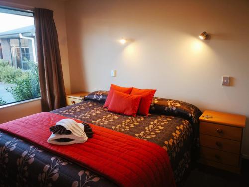 a bedroom with a bed with a red blanket and a window at Aston Court Motel in Blenheim