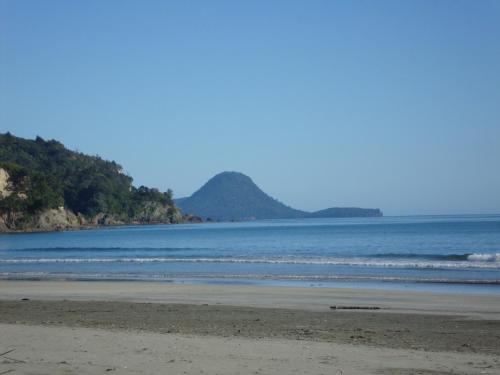 a beach with the ocean and mountains in the background at Beachfront Bliss in Ohope Beach