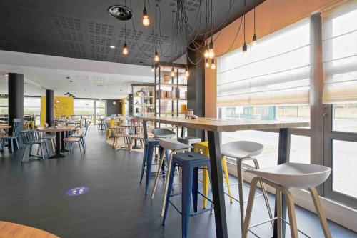 a restaurant with tables and stools in a room with windows at Campanile Roissy - Aéroport CDG - Le Mesnil Amelot in Le Mesnil-Amelot