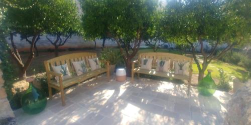 two wooden benches sitting on a sidewalk next to trees at Corte Piri in Tricase