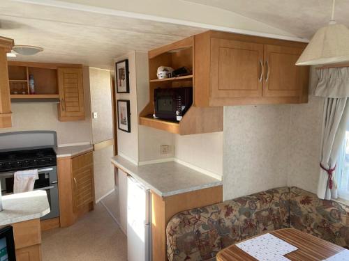 a small kitchen with wooden cabinets and a couch at Eastgate Fantasy Islands Static Caravan Park in Ingoldmells
