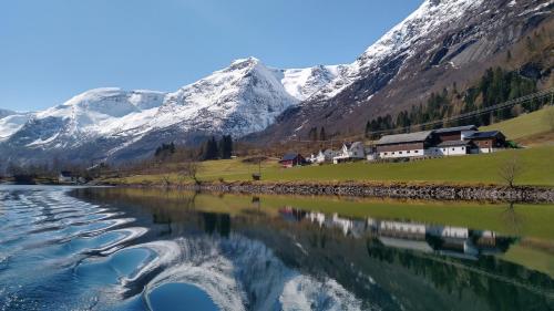 a village on the side of a river with snow covered mountains at Oldevatn Camping in Olden