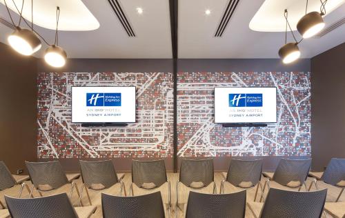 a room with chairs and two screens on a wall at Holiday Inn Express Sydney Airport by IHG in Sydney