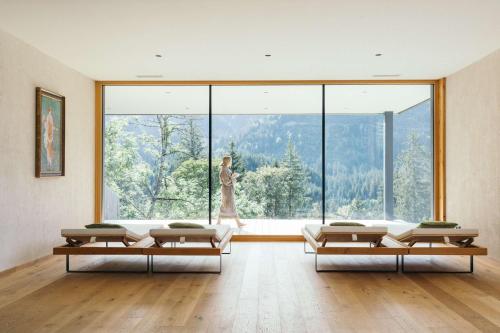 a living room with a woman walking through a large window at Ruhehotel & Naturresort Rehbach - Adults only in Schattwald