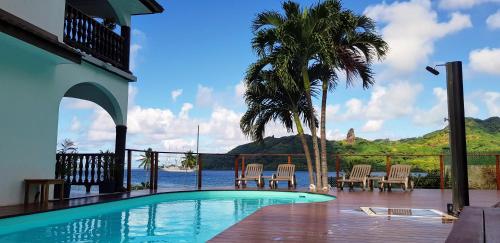 a swimming pool with chairs and a palm tree at Villa Maroe (étage entier, deux chambres, salle de bain et cuisine) in Fare
