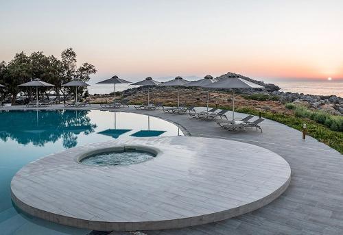 a swimming pool with chairs and umbrellas next to the ocean at Kavos Hotel & Suites in Stavros