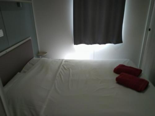 a white bed with two red pillows on it at Bungalow in Canet-en-Roussillon