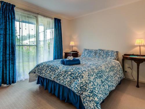 a bedroom with a bed with a blue blanket and a window at Colonnades in Cape Woolamai