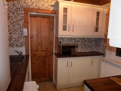 cocina con armarios blancos y puerta de madera en Jane's Cottage Free Parking, en Inverness