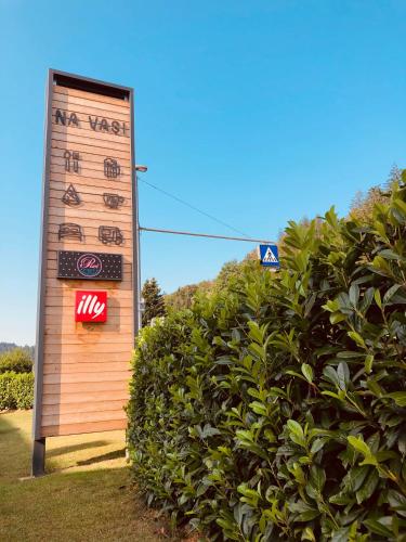 a sign in front of a bush next to a hedge at Na Vasi restavracija in prenočišča in Škofja Loka