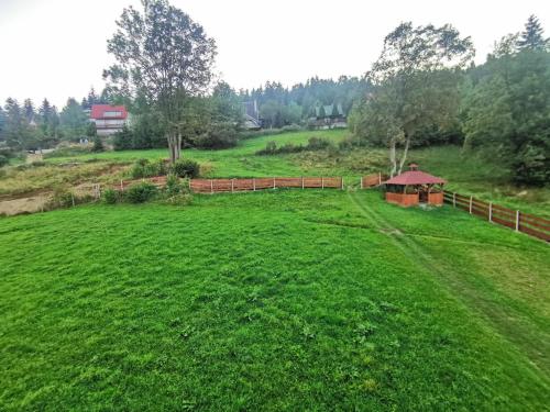 a large green field with a fence and a gazebo at Noclegi "Na Szczyrboku" Dom II in Korbielów