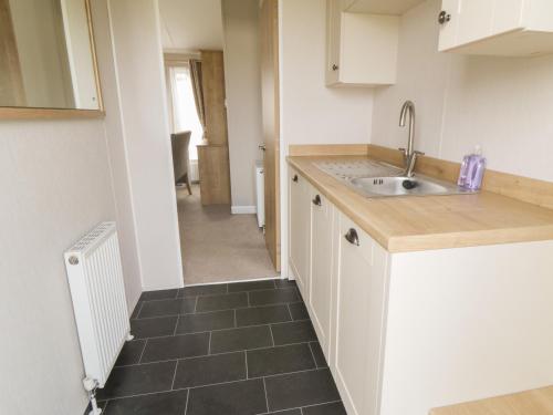 a kitchen with white cabinets and a sink and a hallway at Daisy Lodge in Scarborough