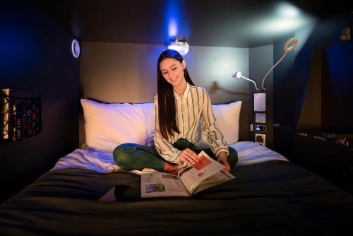 a woman sitting on a bed reading a book at Lublin Capsules - Lubelskie Kapsuły in Lublin