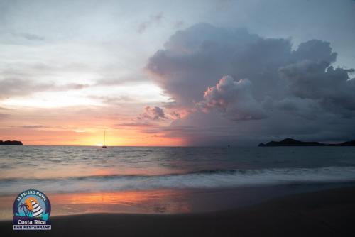 a sunset on the beach with a boat in the water at Hotel El Velero in Playa Hermosa