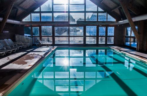 a swimming pool with blue water in a building with windows at Flocons du Soleil by Actisource in La Joue du Loup