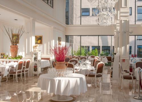 een restaurant met witte tafels en stoelen en een kroonluchter bij Grand Hotel Palladium in München