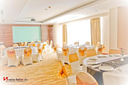 a conference room with white tables and chairs and a screen at Swiss-Belinn SKA Pekanbaru in Pekanbaru
