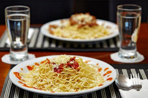 two plates of pasta on a wooden table with glasses at Sokratis Hotel in Nea Moudania