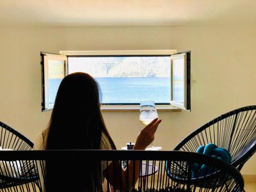 a woman sitting at a table looking out a window at the ocean at Apartments Mare in Korčula