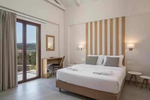 a bedroom with a bed and a desk and a balcony at Spilia Village Hotel & Villas in Spiliá