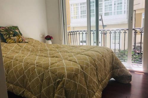 ein Bett mit einer Bettdecke in einem Schlafzimmer mit einem Balkon in der Unterkunft Precioso loft en el centro in A Coruña