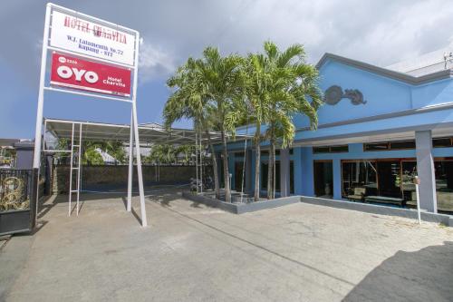 a sign in front of a blue building with palm trees at SUPER OYO 2320 Hotel Charvita in Kupang