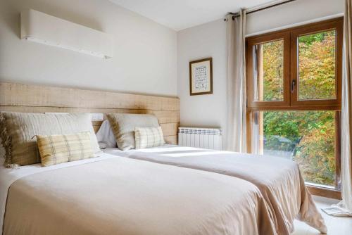 a white bedroom with two beds and a window at MONTELIA Ático El Ciervo de Panticosa in Panticosa