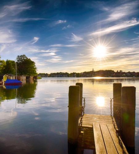 a dock on a lake with the sun in the sky at Ferienwohnung Urlaub mit Pferd, Hof Müggenburg in Stüdenitz