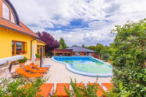 a swimming pool with orange chairs next to a house at Hotel Mayer Alsóörs in Alsóörs