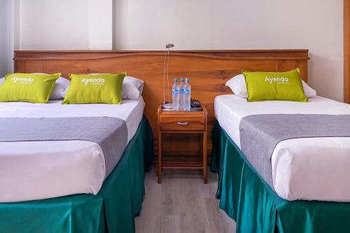 two beds in a hotel room with bottles on a night stand at Ayenda 1140 Roma Plaza in Manizales