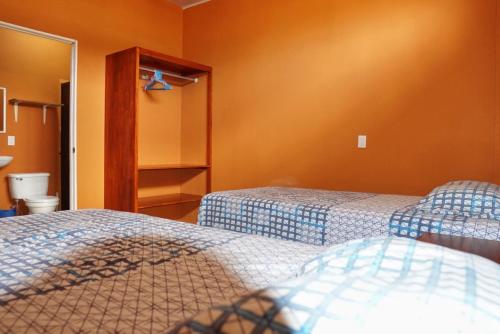 two beds in a room with orange walls at Hotel Heliconia Los Chiles in Los Chiles