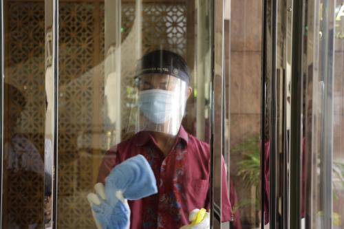 a man wearing a mask and gloves looking through a window at Ambhara Hotel in Jakarta