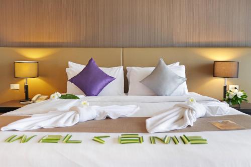 Elle comprend un grand lit avec des draps blancs et des oreillers violets. dans l'établissement Mida Hotel Don Mueang Airport, à Bangkok