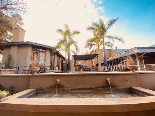 a large fountain in front of a house with palm trees at Old Mine Guesthouse in Musina