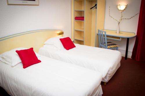 2 Betten in einem Hotelzimmer mit roten Kissen in der Unterkunft Le Terminus in Tarascon