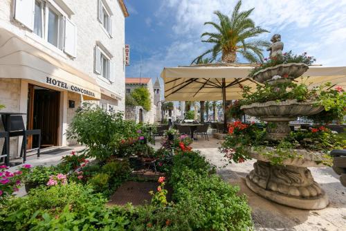 a garden with flowers and a fountain with an umbrella at Hotel Concordia in Trogir