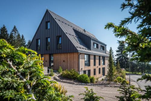 a house with a black roof on a hill with trees at Hotel Královka in Bedřichov