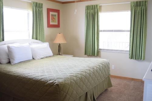 a bedroom with a bed and two windows with green curtains at Ocean Landings Resort in Cocoa Beach