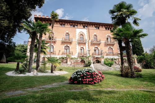 un grande edificio in mattoni con palme e fiori di Hotel Bellevue a Gardone Riviera