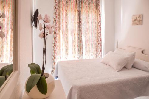 Un dormitorio con una cama blanca y un jarrón con una flor en Pensión Las Palmas en Carboneras