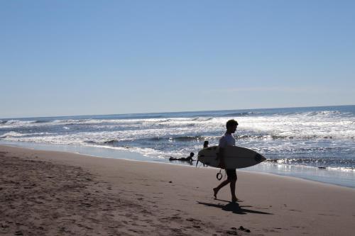 a man walking on the beach with a surfboard at Olas Permanentes El Zonte in El Zonte