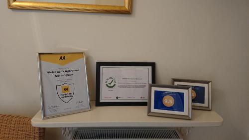 a shelf with three certificates and pictures on it at Violet Bank Apartment Morningside in Edinburgh