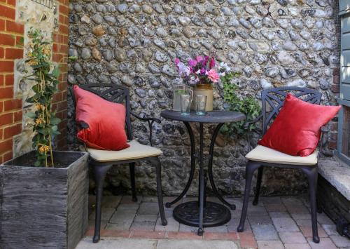 two chairs and a table with red pillows on a patio at Providence Cottage a Sussex boutique retreat for two in Angmering