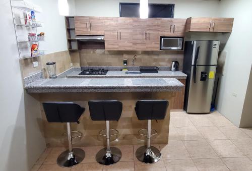 a kitchen with a counter with a refrigerator and stools at NCG SUITE SAMANES in Guayaquil