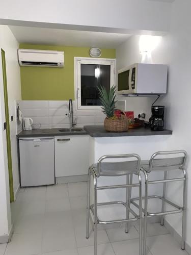 a kitchen with white cabinets and a counter with two stools at Superbe Studio Ultra COSY à 2 min de la PLAGE in Sainte-Anne