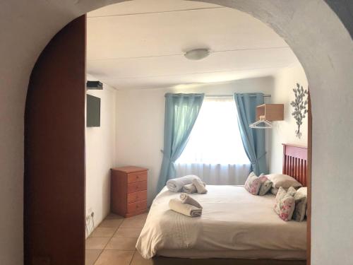 a bedroom with a bed with blue curtains and a window at La Bella B&B Under The Fig Tree in Bela-Bela